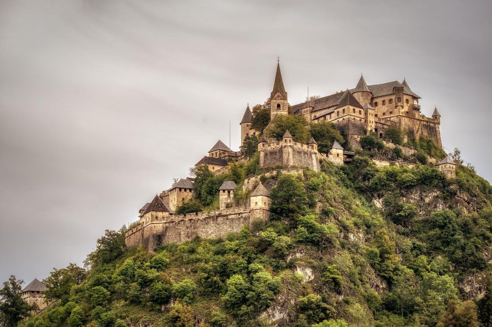 Fotka zobtazuje európsky hrad postavený na vysokom kopci na ktorom sú stromy.