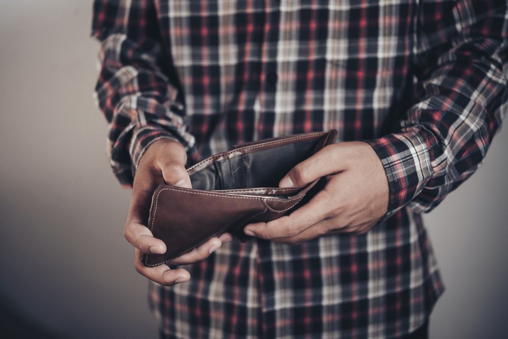 Fotka zobrazuje osobu, ktorá drží svoju vyprádnenú peňaženku a má oblečenú košeľu.