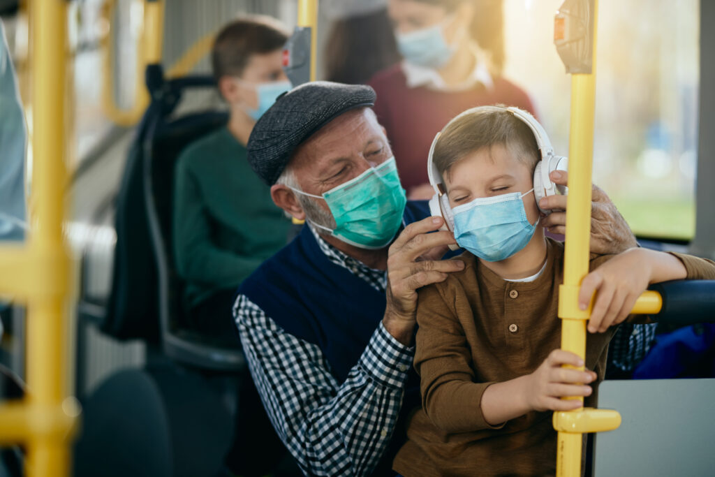 Šťastný vnuk počúva hudbu cez slúchadlá počas cestovania autobusom s dedkom počas pandémie koronavírusu.